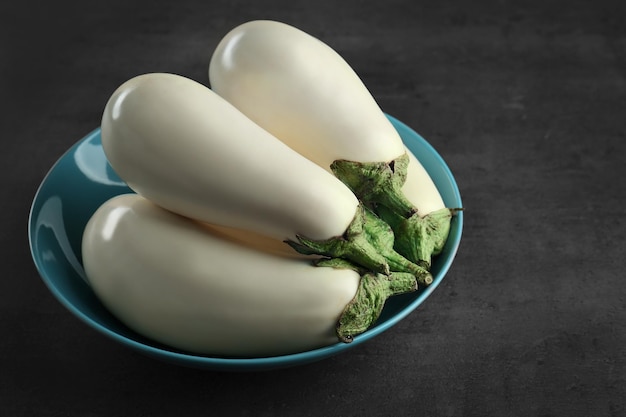 Plate with fresh white aubergines on grey background