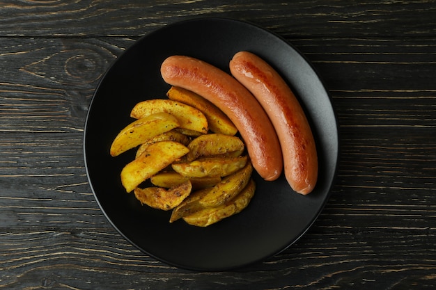 Plate with fried potato and sausage on wooden background