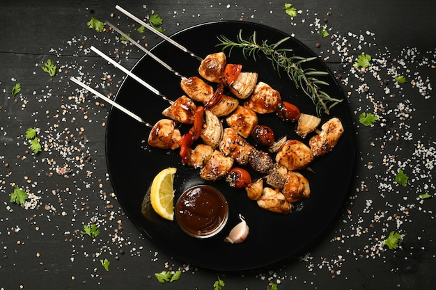 Plate with grilled chicken meat skewers and barbecue sauce on black rustic wooden table