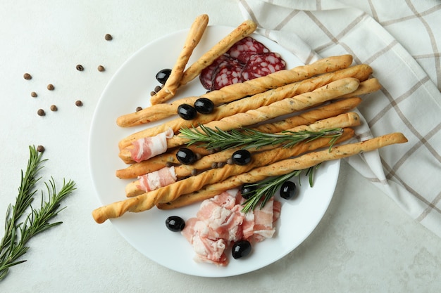 Plate with grissini and snacks on white textured background