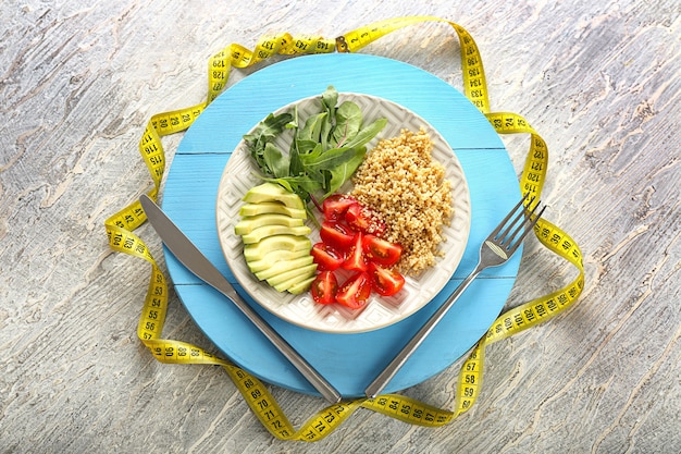 Plate with healthy fresh salad and measuring tape on wooden board. diet concept