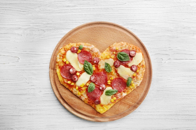 Plate with heartshaped pizza on wooden background