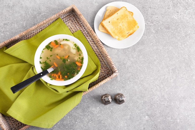 Plate with homemade chicken soup on wicker tray