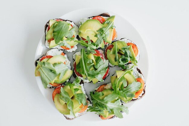 Plate with homemade toasts with avocado on modern white kitchen sandwich made of whole grain bread avocado tomato arugula and cheese top view home cooking concept