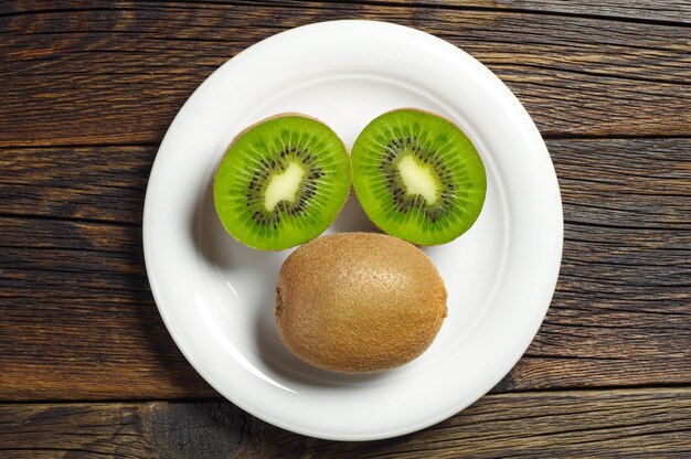 Plate with kiwi fruit and half on dark wooden background, top view