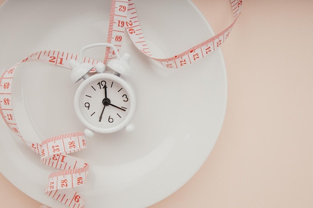 Plate with measuring tape and alarm clock on pink background Concept diet healthy food and meal plan