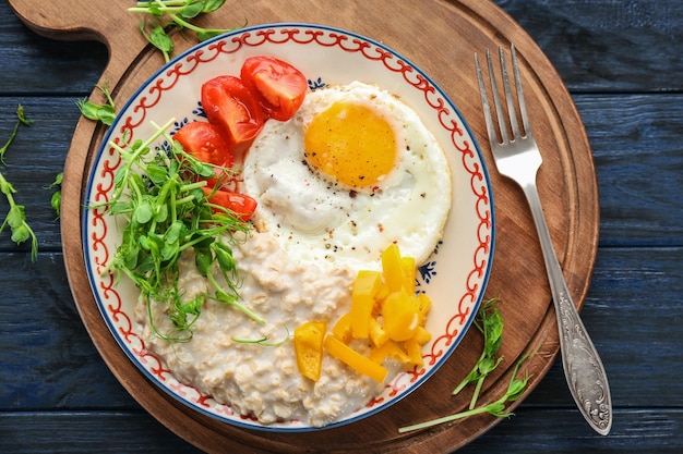 Plate with oatmeal porridge fried egg and garnish on wooden board