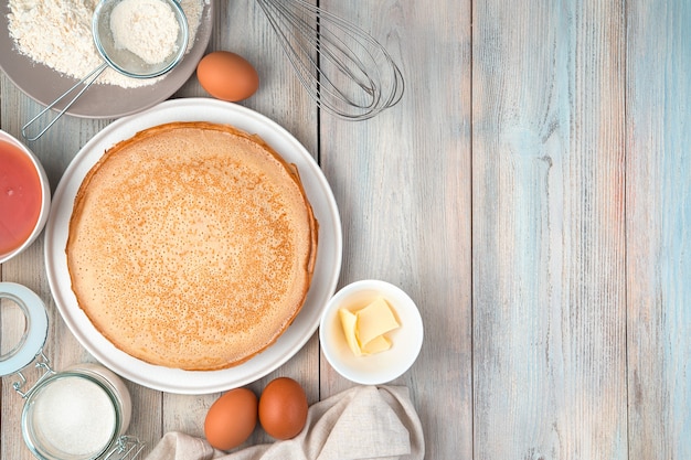 Plate with pancakes, eggs, flour, butter, honey on a light background.
