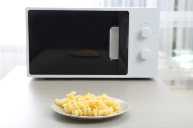 Photo plate with pasta and cheese near microwave on table