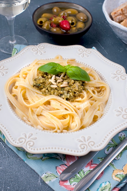 plate with pasta with pesto sauce and olives on a stone background