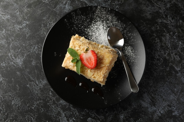 Plate with piece of Napoleon cake with strawberry on black smokey surface