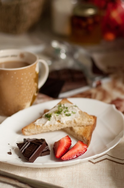Тарелка с кусочками шоколада, клубники и тостов на размытом фоне