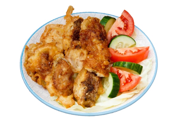 Plate with pieces of fried fish and freshly sliced tomatoes and cucumbers on white isolated background