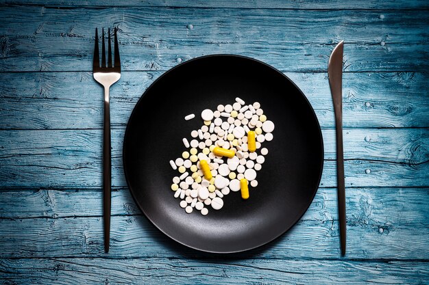 Plate with pills on wooden background flat lay