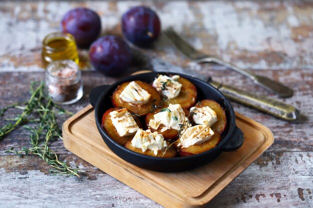 Plate with plum halves baked with feta cheese and herbs on a shabby wooden surface