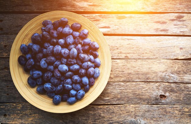 Plate with plums on a rustic wooden background, top view.