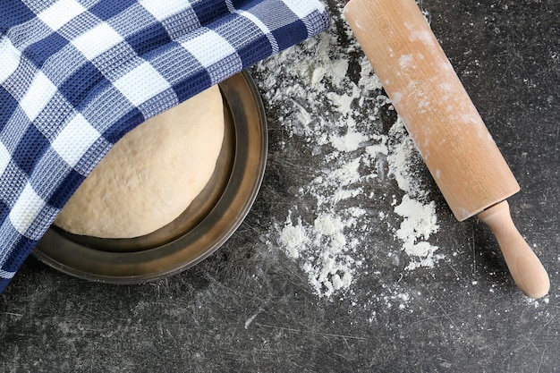 Plate with raw dough under napkin and rolling pin on table