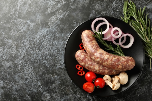 Plate with raw sausage and ingredients on black smokey