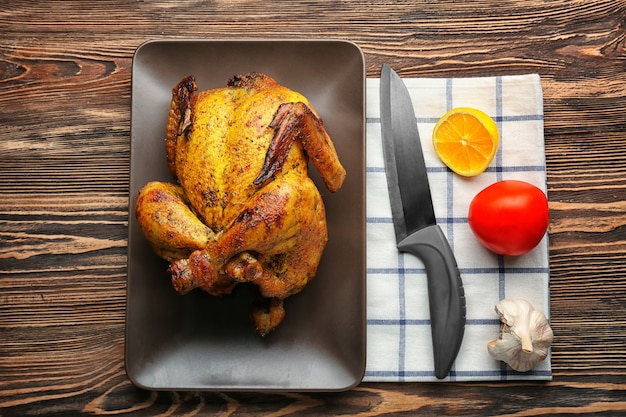 Plate with roasted beer can chicken on wooden background