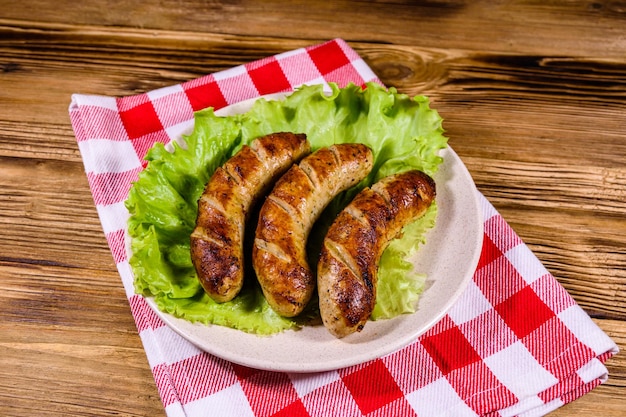 Plate with roasted sausages and lettuce leaves on a wooden table