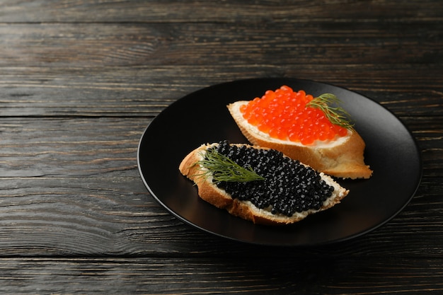 Foto piastra con panini con caviale su sfondo di legno, spazio per il testo