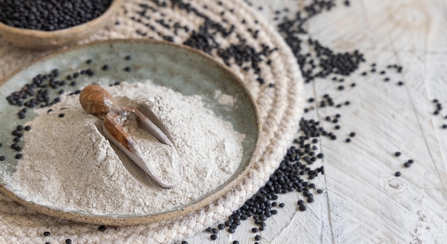 Plate with a scoop of black lentils flour and beans on white wooden table close up with copy space.  Alternative flour, healthy eating and vegetarian concept. Traditional Asian and North African cuisi