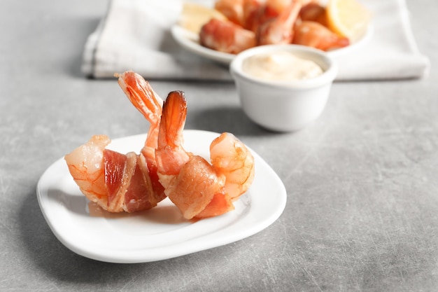 Plate with shrimps wrapped in bacon on table closeup