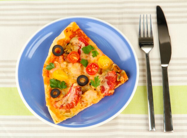 Plate with a slice of delicious pizza on tablecloth closeup