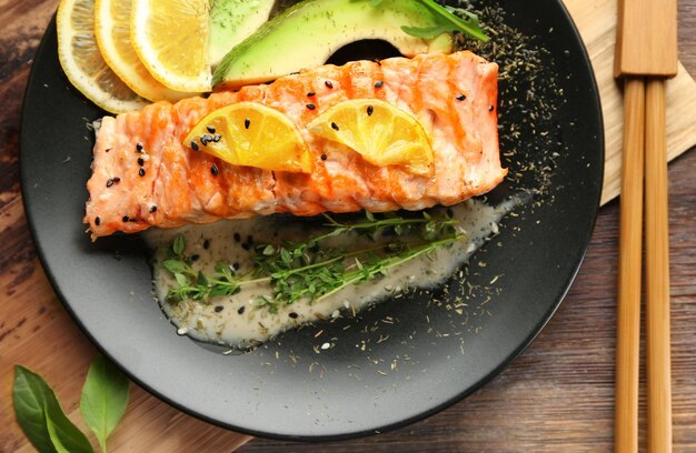 Plate with slice of delicious salmon and fish sauce on table