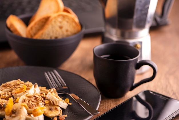 Plate with sliced banana, granola, candied fruit and honey, toast and cup of coffee