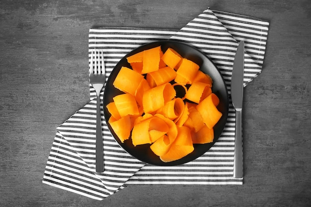 Plate with sliced carrot and striped napkin on table