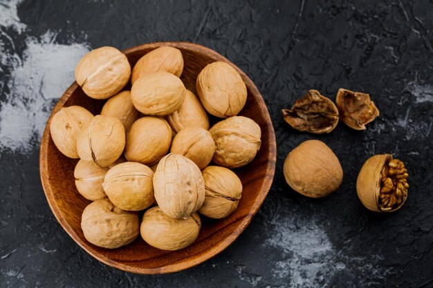 Plate with some raw walnuts and peel on dark background