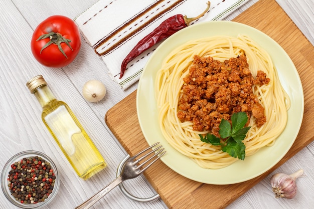 Фото Тарелка со спагетти болоньезе и ингредиентами для приготовления. стеклянная миска с душистым перцем, бутылка масла, чеснок, перец чили и помидор. вид сверху.