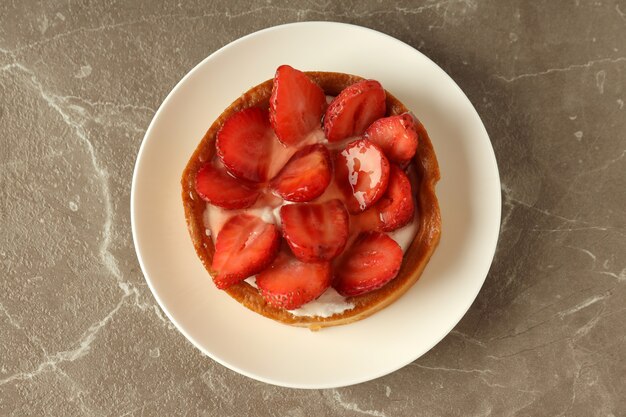 Plate with strawberry tart on gray textured table.