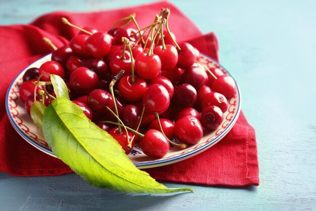 Plate with sweet cherries on color background