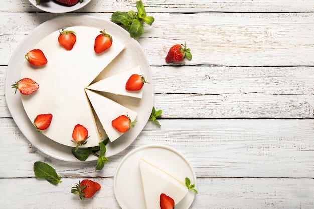 Plate with tasty cheesecake with strawberries and mint on a wooden background. View from above