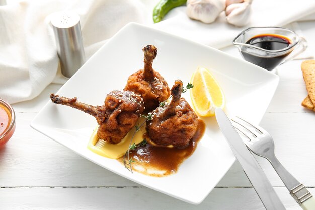 Plate with tasty chicken lollipops on light wooden surface