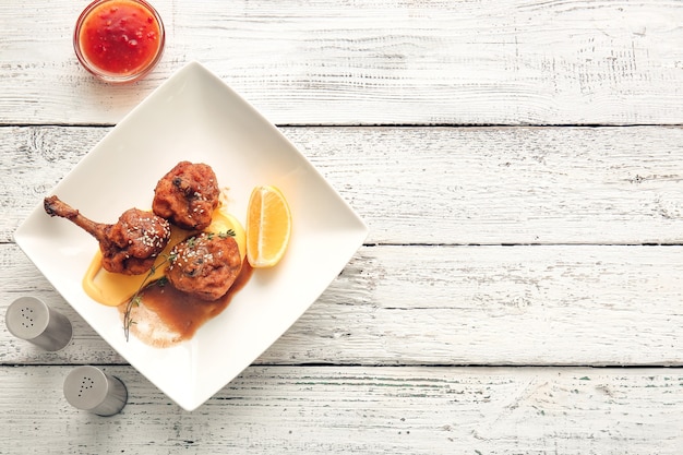 plate with tasty chicken lollipops on light wooden surface