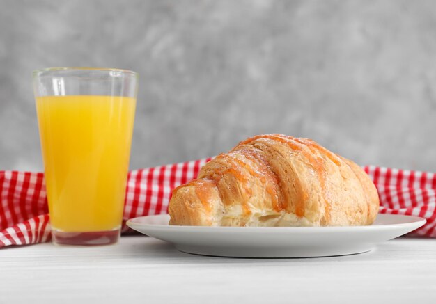 Plate with tasty croissant and glass of juice on table