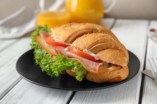 Plate with tasty croissant sandwich on table