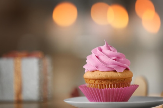 Plate with tasty cupcake on table against blurred background