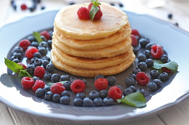 Plate with tasty pancakes and berries on wooden table close up view