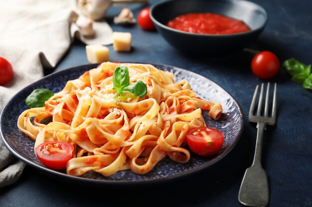 Plate with tasty pasta and tomato sauce on dark background