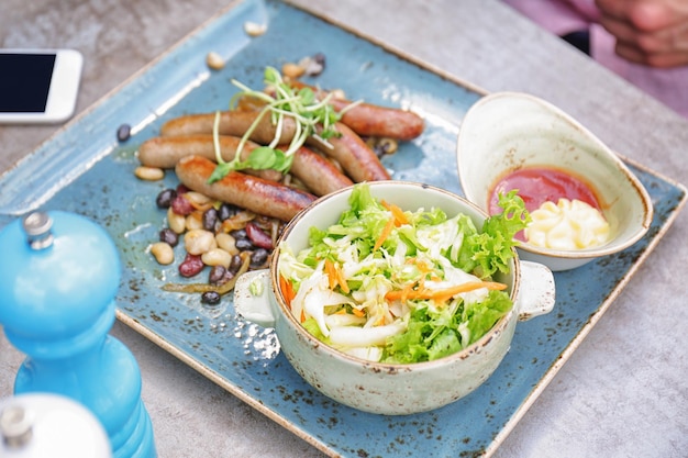 Plate with tasty sausages and salad on table