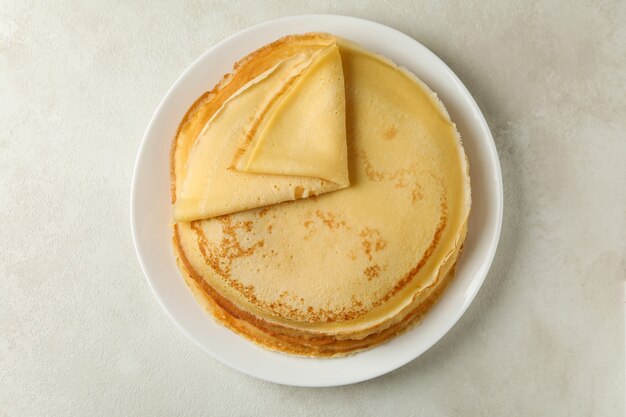 Plate with thin pancakes on white textured background