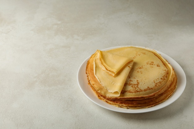 Plate with thin pancakes on white textured background