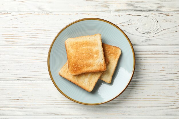 Plate with toasts on white wooden background, top view