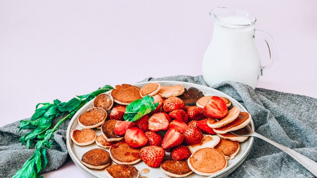 전통적인 팬케이크와 딸기와 민트 잎을 가진 작은 팬케이크 시리얼 접시. 트렌디 한 음식. 미니 시리얼 팬케이크