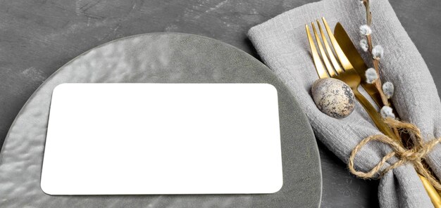 Photo plate with white blank sheet golden cutlery quail egg willow twig on gray banner mock up close up