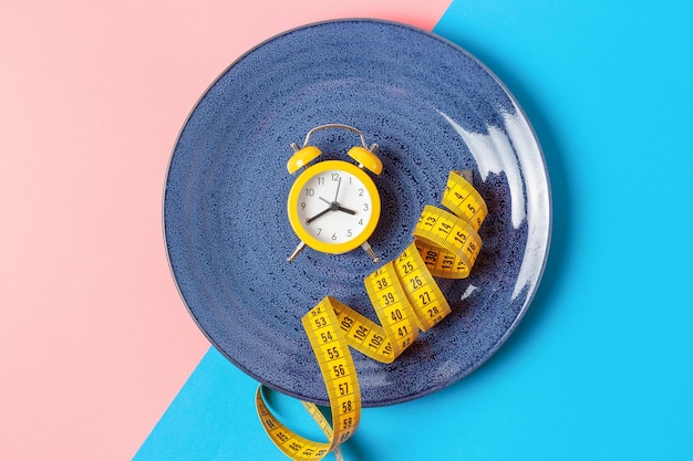 a plate with yellow alarm clock and measuring tape on a blue and pink background